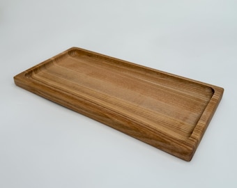 May include: A long, rectangular wooden tray with a slightly raised edge. The tray is made of light brown wood with a natural grain pattern.