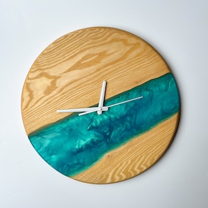 May include: A round wooden clock with a teal blue epoxy resin river design. The clock has white hands and a white centre.
