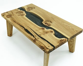 May include: A wooden coffee table with a natural wood finish and a black epoxy river running through the center. The table has four legs and is made of solid wood.