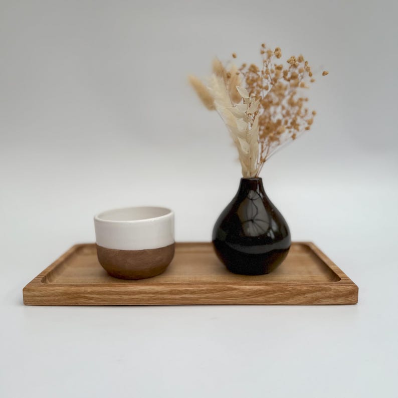 May include: A wooden tray with a white and brown ceramic cup and a black ceramic vase with dried flowers.