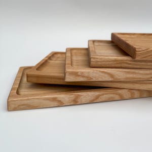 May include: Four wooden trays of varying sizes stacked on top of each other. The trays are made of light brown wood with a natural grain pattern.