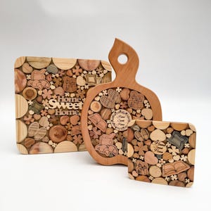 May include: Three wooden chopping boards with a mosaic design of small wood pieces in various shapes and sizes. The largest board is shaped like an apple and has the text "Home Sweet Home" engraved on it. The other two boards are square and have the text "Home Sweet Home" engraved on them.
