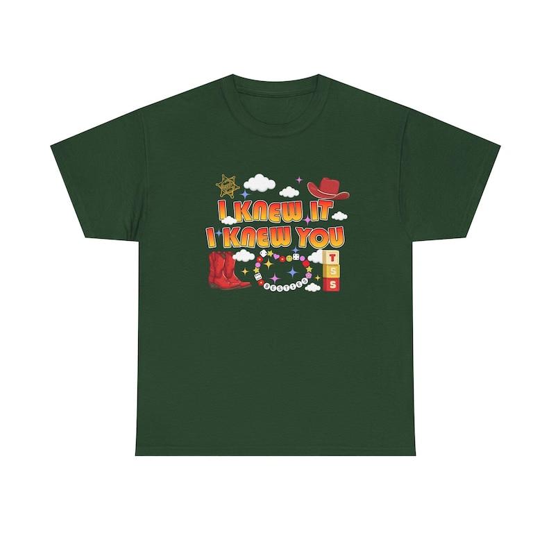 May include: A dark green short-sleeve t-shirt featuring a graphic print with the text I KNEW IT I KNEW YOU. The design includes a red cowboy hat, a red cowboy boot, a sheriff star, white clouds, colorful beads, and stacked blocks with letters.