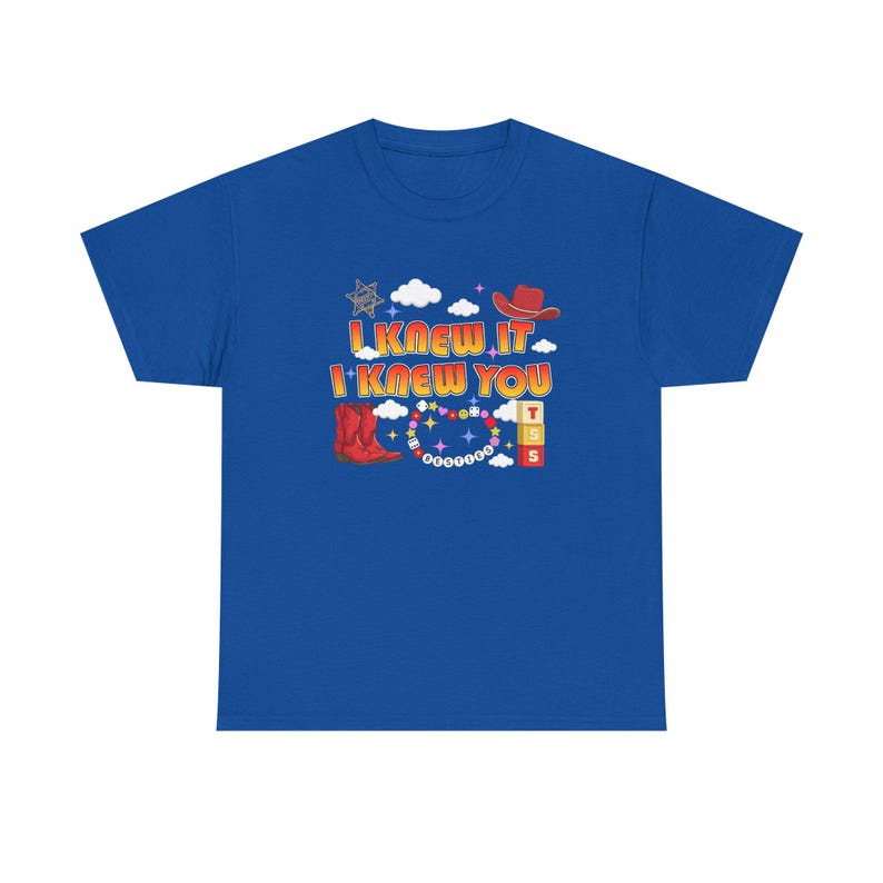 May include: A royal blue short-sleeve t-shirt featuring a graphic print with the text I KNEW IT I KNEW YOU. The design includes red cowboy boots, a red cowboy hat, a sheriff star, white clouds, colorful beads, and stacked blocks with letters.