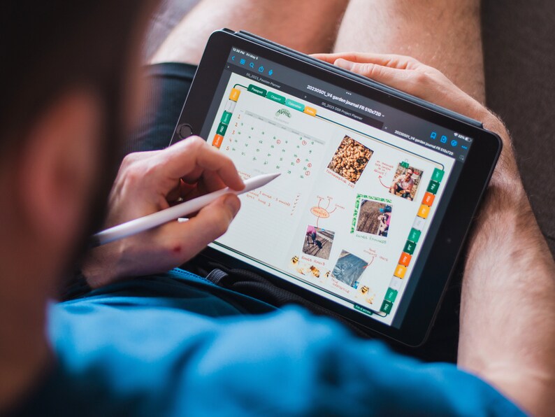 May include: A person using a digital tablet to plan a garden. The tablet screen shows a calendar, photos, and handwritten notes. The text on the screen reads "2023/06/01 - 2023/06/30 Garden Planner for 2023".