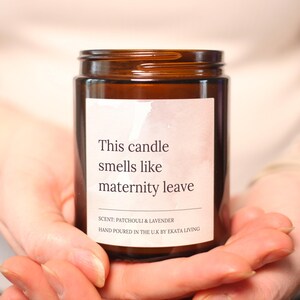 May include: A brown glass jar candle with a white label. The label reads "This candle smells like maternity leave." The scent is patchouli and lavender. Hand-poured in the U.K. by Ekata Living.
