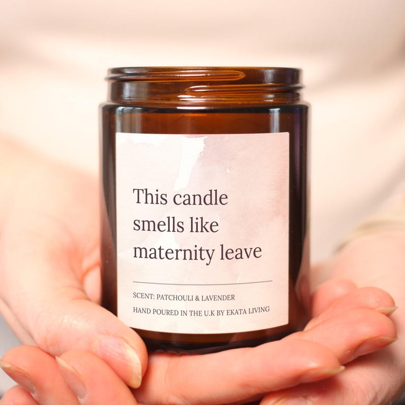 May include: A brown glass jar candle with a white label. The label reads "This candle smells like maternity leave." The scent is patchouli and lavender. Hand-poured in the U.K. by Ekata Living.