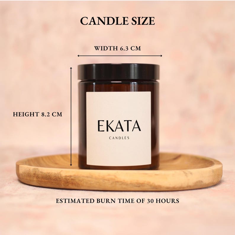 May include: A brown glass candle jar with a black lid, labeled "EKATA CANDLES." The candle is 8.2 cm tall and 6.3 cm wide. The estimated burn time is 30 hours. The candle sits on a wooden tray.