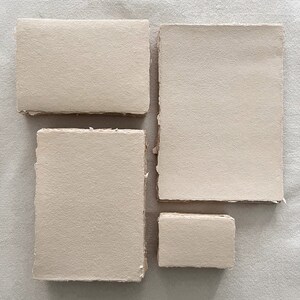 May include: Four pieces of handmade, textured paper in varying rectangular shapes. The paper has a neutral, beige colour and a rough, deckled edge. The arrangement includes two rectangles and two squares, all with a natural, organic aesthetic.