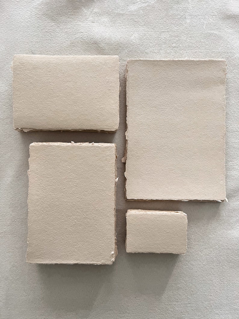 May include: Four pieces of handmade, textured paper in varying rectangular shapes. The paper has a neutral, beige colour and a rough, deckled edge. The arrangement includes two rectangles and two squares, all with a natural, organic aesthetic.
