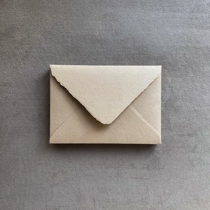 May include: A small, beige envelope with a deckled edge, centered on a gray background. The envelope is rectangular with a pointed flap. The paper has a slightly textured appearance. Ideal for stationery, invitations, or small notes.