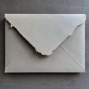May include: A light gray envelope with a textured surface and a torn edge. The envelope is closed, with the flap folded over. The background is a darker gray.