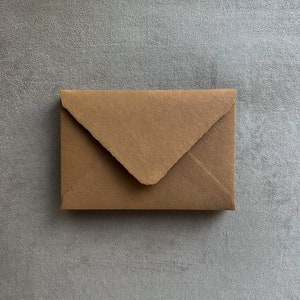 May include: A small, brown paper envelope with a triangular flap closure. The envelope is rectangular and appears to be made of textured, recycled paper. The background is a solid, gray surface.