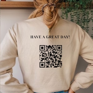 May include: A beige sweatshirt with the text "HAVE A GREAT DAY!" and a black and white QR code printed on the back.
