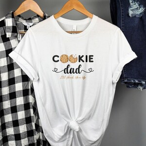 May include: White t-shirt with the text "Cookie Dad" and two chocolate chip cookies. The text below the cookies says "I'll love you forever".