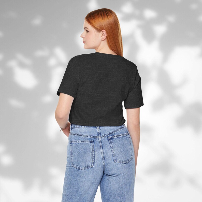 May include: Dark gray crop top with a V-neck. The shirt is paired with light blue denim jeans. The model is facing away from the camera, with a neutral background.