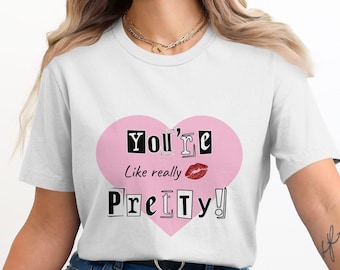 May include: White t-shirt with a pink heart graphic that says "You're like really Pretty!" in black text with a red lip print inside the heart.