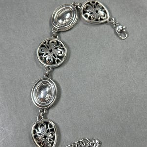 以下が含まれることがあります： 楕円形と円形の装飾的なリンクが特徴のシルバーカラーのブレスレット。 ブレスレットはロブスタークラスプ留め具で、透かし彫りのフローラルデザインが含まれています。 ブレスレットは光沢のある金属素材で作られています。