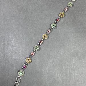 May include: A silver-toned bracelet featuring a series of colorful flower-shaped charms. Each charm is adorned with a cluster of small, sparkling gemstones in shades of pink, yellow, green, and red. The bracelet has a lobster clasp closure.