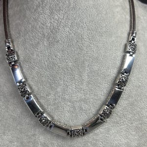 Peut inclure: Collier argent&eacute; compos&eacute; de maillons rectangulaires et carr&eacute;s. Les maillons rectangulaires sont lisses, tandis que les carr&eacute;s pr&eacute;sentent un motif floral. Le collier a une cha&icirc;ne souple de type serpent. Longueur approximative 40 cm.