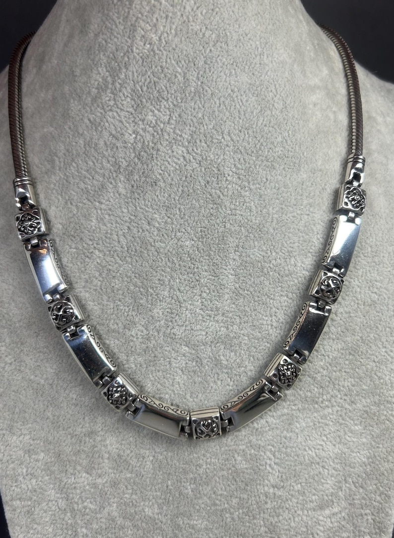 Peut inclure: Collier argent&eacute; compos&eacute; de maillons rectangulaires et carr&eacute;s. Les maillons rectangulaires sont lisses, tandis que les carr&eacute;s pr&eacute;sentent un motif floral. Le collier a une cha&icirc;ne souple de type serpent. Longueur approximative 40 cm.