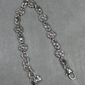 May include: Silver-toned bracelet featuring a floral design. The bracelet has multiple flower-shaped links connected by smaller circular links. It includes a lobster clasp closure and an adjustable chain.