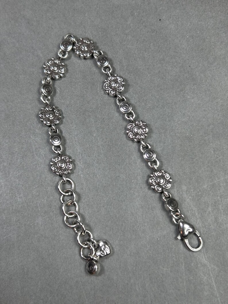May include: Silver-toned bracelet featuring a floral design. The bracelet has multiple flower-shaped links connected by smaller circular links. It includes a lobster clasp closure and an adjustable chain.