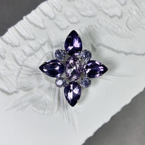 Vintage korsformad heraldisk silverfärgad brosch med rosa och lila fasetterade kristaller.