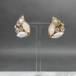 May include: A pair of vintage-style earrings. Each earring features a gold-toned frame encasing a cluster of clear and white gemstones. The design includes teardrop-shaped white stones and smaller, sparkling accents, creating a glamorous look.