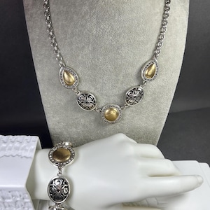 Peut inclure: Ensemble collier et bracelet argent&eacute;. Le collier pr&eacute;sente des accents dor&eacute;s en forme de goutte et d'ovale, ainsi que des motifs circulaires en filigrane. Le bracelet reprend le design du collier, avec des d&eacute;tails dor&eacute;s et en filigrane. Les bijoux sont pr&eacute;sent&eacute;s sur un mannequin.