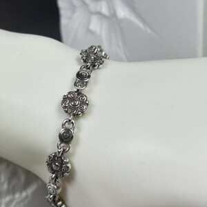 May include: Silver-toned bracelet featuring a series of floral and circular links. The bracelet is composed of multiple decorative flower-shaped elements, connected by smaller circular links. The design has an antique or vintage aesthetic.