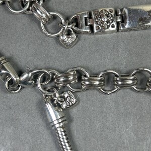 Peut inclure: Gros plan sur deux bracelets argent&eacute;s. L'un comporte un charm en forme de c&oelig;ur avec un motif grav&eacute; et un fermoir floral. L'autre pr&eacute;sente un motif de cha&icirc;ne serpent et un charm en forme de c&oelig;ur.