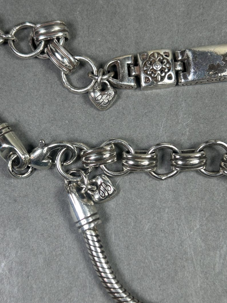 Peut inclure: Gros plan sur deux bracelets argent&eacute;s. L'un comporte un charm en forme de c&oelig;ur avec un motif grav&eacute; et un fermoir floral. L'autre pr&eacute;sente un motif de cha&icirc;ne serpent et un charm en forme de c&oelig;ur.