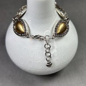 以下が含まれることがあります： ゴールドカラーのしずく型アクセントが付いたシルバーカラーのブレスレット。各しずくは、小さな透明なクリスタルで縁取られています。ブレスレットには、サイズ調整用のチェーンエクステンションとロブスタークラスプが付いています。