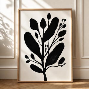 Op de afbeelding: Een ingelijste wandkunstprint met een gedurfde, effen zwarte botanische illustratie van een bladrijke plant met ronde bladeren en kleine knoppen op een effen gebroken witte achtergrond, gevat in een eenvoudige lichtgekleurde houten lijst.