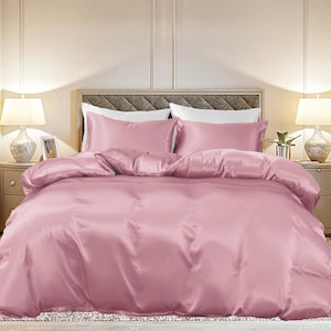 May include: A pink satin duvet cover and pillowcase set. The bedding is smooth and luxurious, with a soft sheen.