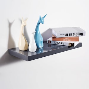 May include: A grey floating shelf with three ceramic sculptures and a stack of books. The books are titled "CRAFT", "NATURALE", and "Dentro di te".