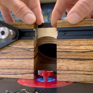 May include: A woodworking router table with a zebrawood finish. The table features a black metal guide and a red base with the text "Made in Canada". The image shows the table being assembled.