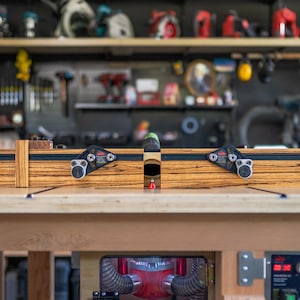 May include: A wooden woodworking router with black and silver hardware. The router is set on a wooden workbench, with tools and equipment visible in the background. The router has a black and silver rail system.