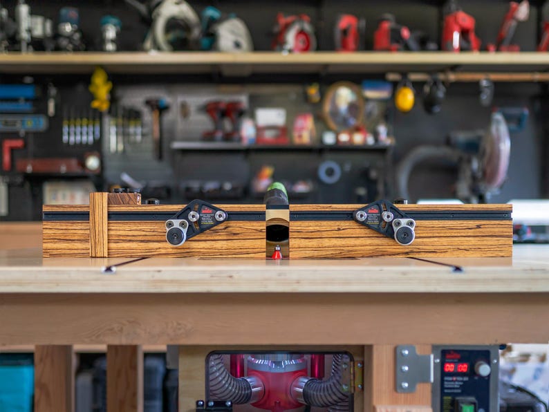 May include: A wooden woodworking router with black and silver hardware. The router is set on a wooden workbench, with tools and equipment visible in the background. The router has a black and silver rail system.