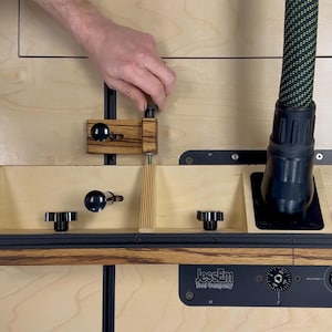 May include: A woodworking router table with a wooden fence, black knobs, and a dust collection hose. The table features a black base with the "JessEm Tool Company" logo. A hand is adjusting a part of the table.