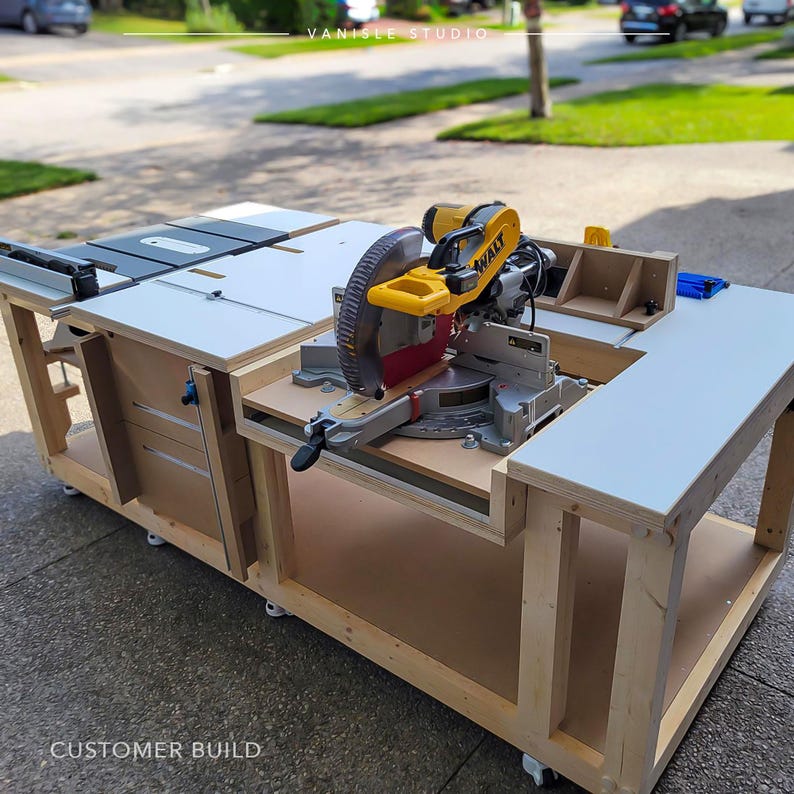 May include: A large wooden workbench featuring a yellow and black DeWalt mitre saw mounted on the surface. The workstation includes a white tabletop, integrated storage drawers, and caster wheels. The text VANISLE STUDIO and CUSTOMER BUILD appear.