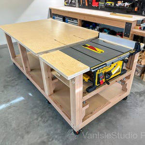 May include: A large wooden workbench with a built-in yellow and black DEWALT table saw. The workbench has a light wood finish and is on wheels. The saw has a red and yellow blade guard. The workbench is designed for woodworking.
