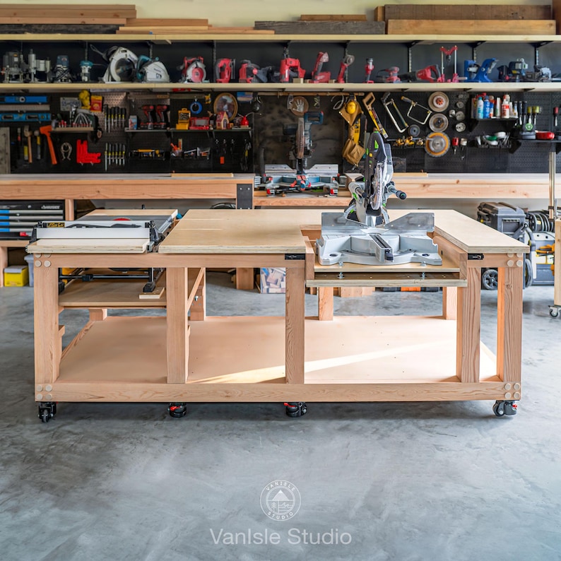 May include: A large, light-coloured wooden workbench on wheels featuring a built-in table saw on the left and a mitre saw integrated into the right side. The structure includes a lower storage shelf and a flat, expansive plywood work surface.