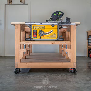 May include: A yellow DeWalt table saw mounted into a custom-built wooden workbench with a light brown finish. The workbench features a lower shelf, sturdy legs, and four black swivel casters at the base for mobility in a workshop setting.