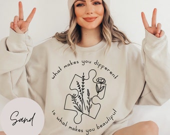May include: A beige sweatshirt with a black graphic of a puzzle piece with flowers inside. The text around the puzzle piece reads "what makes you different is what makes you beautiful".