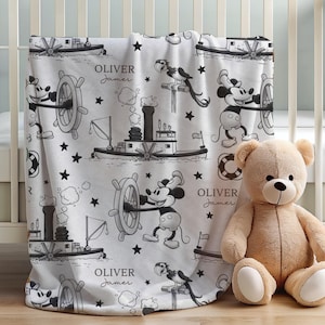 May include: A white fleece blanket featuring a black and white pattern of Mickey Mouse steering a steamboat, a parrot, life preservers, and stars. The text "OLIVER James" is printed in a script font throughout the repeating nautical design.