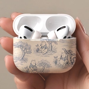 May include: White wireless earbuds in an open case with a Winnie the Pooh design. The case has a beige background with blue illustrations of Winnie the Pooh, Piglet, and Tigger. The earbuds are white.