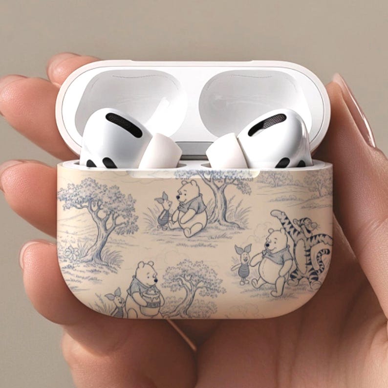 May include: White wireless earbuds in an open case with a Winnie the Pooh design. The case has a beige background with blue illustrations of Winnie the Pooh, Piglet, and Tigger. The earbuds are white.