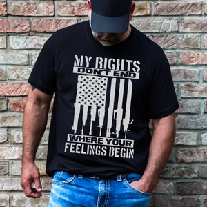 Puede incluir: Una camiseta negra con un diseño gráfico blanco que presenta una bandera estadounidense con armas detrás. El texto en la camiseta dice "Mis derechos no terminan donde tus sentimientos comienzan."